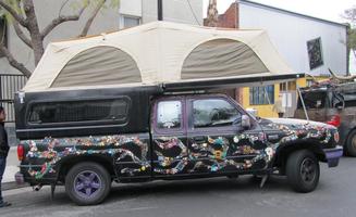 Pickup truck and camper shell with small artistic objects on side and tent on roof carrier