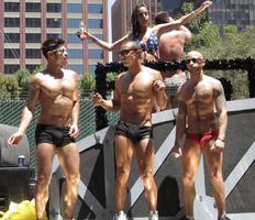 Three male dancers in speedos and one female dancer in bikini in background