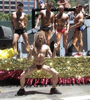 four male dancers in background; blonde-haired man in thong in foreground